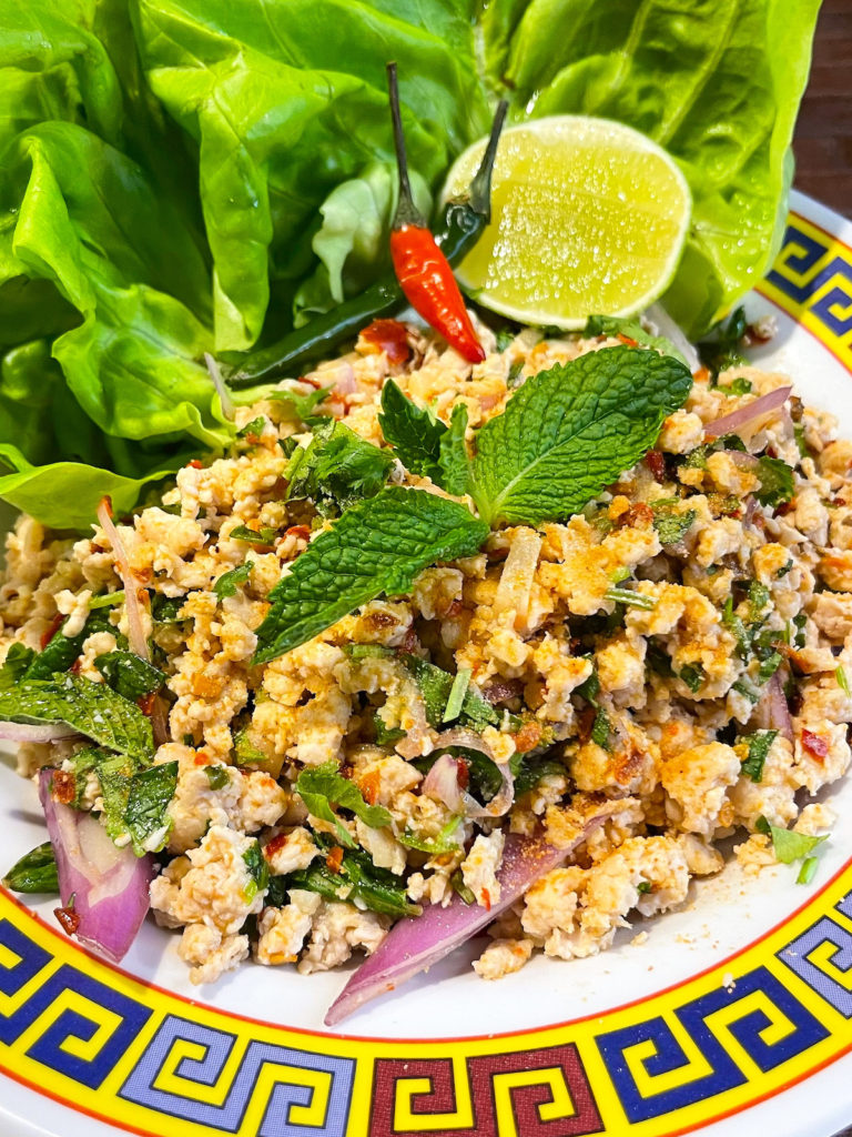 chicken larb / laab on a plate garnished with thai chili peppers, mint and cilantro